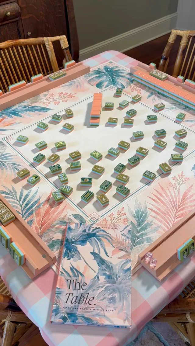 The Table scorebook styled on a pink tropical Mahjong table with tiles and racks